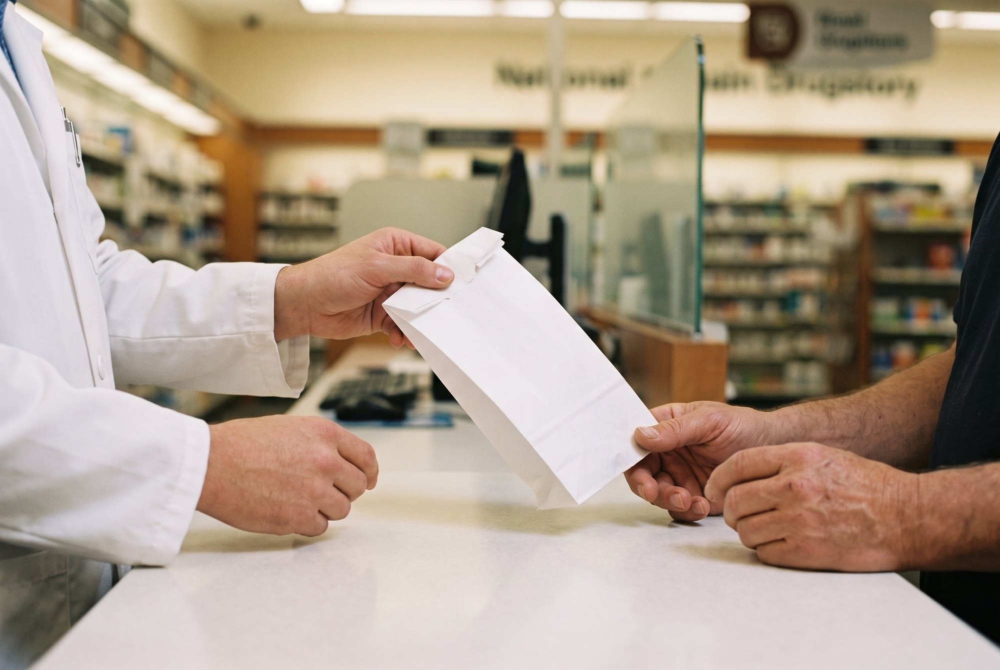 A prescription handed across a pharmacy counter, the texture that proves the rent is working.